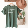 an inspirational t-shirt on a hanger with hat & flowers -moss green color with white screen anything is possible