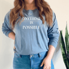 Woman wearing a long sleeve inspirational tee in blue jean color - screen says anything is possible