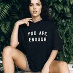 Model sitting down wearing You Are Enough Motivational Black Short Sleeve Shirt (Unisex) in black color