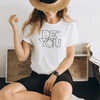 Model sitting on ground in Be you inspirational t shirt in white color with black graphics