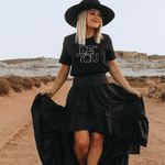 A blonde woman wearing a black inspirational t-shirt with white graphics Be You in the desert